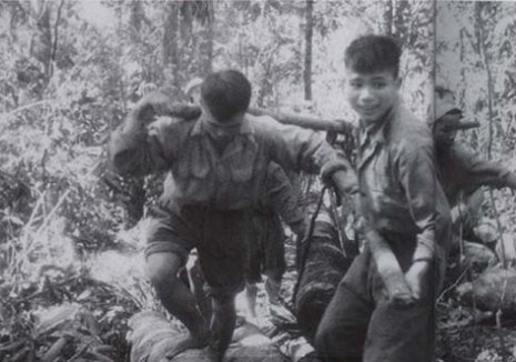 Soldiers carrying supplies using shoulder poles through the jungle