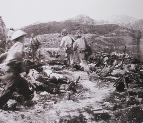 Soldiers advancing through a battlefield trench system past fallen casualties