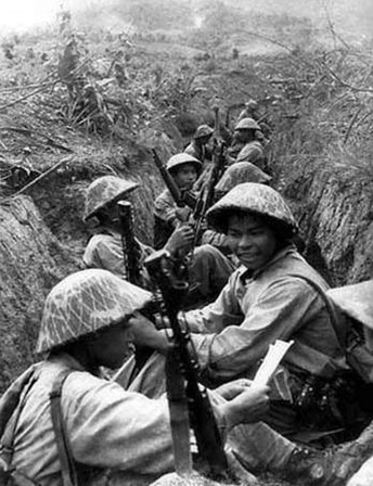 Viet Minh soldiers sitting in a trench, with one reading a document.